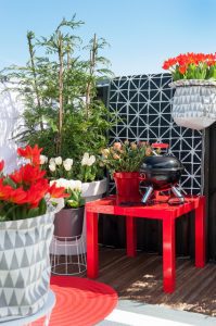 a red table with a grill and flowers in pots